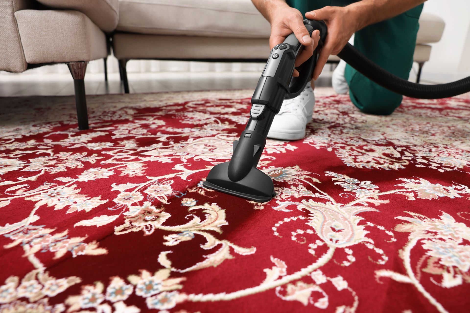 Person vacuuming a red patterned carpet in a living room