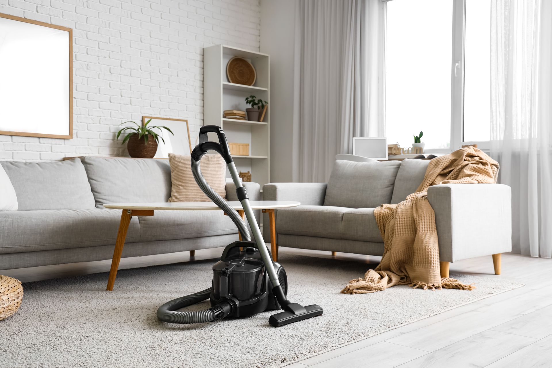 Living room with gray sectional sofa, vacuum cleaner, and gold throw blanket on a light rug