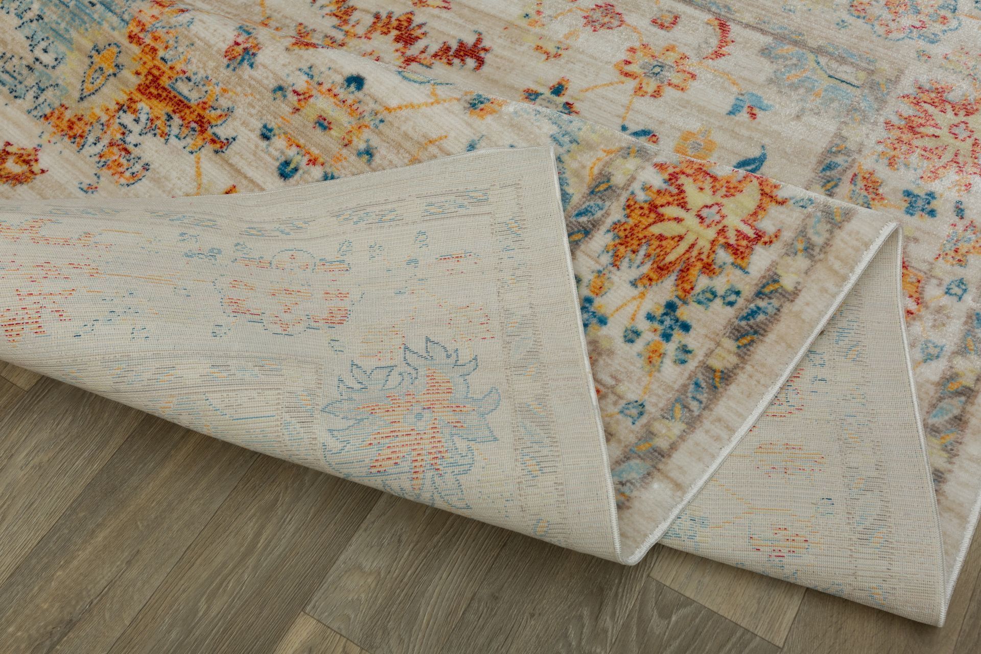 Rolled corner of a light floral rug on a wooden floor, showing beige backing and multicolor pattern
