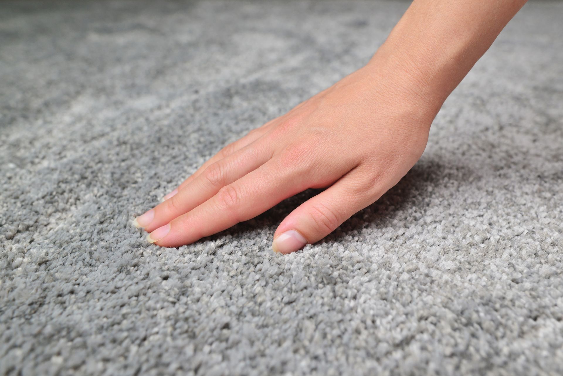 Hand touching a gray textured carpet surface