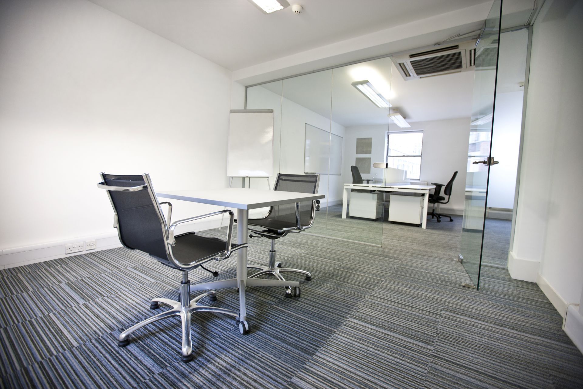 Modern office meeting room with glass walls, white desk, and black chairs on a carpeted floor