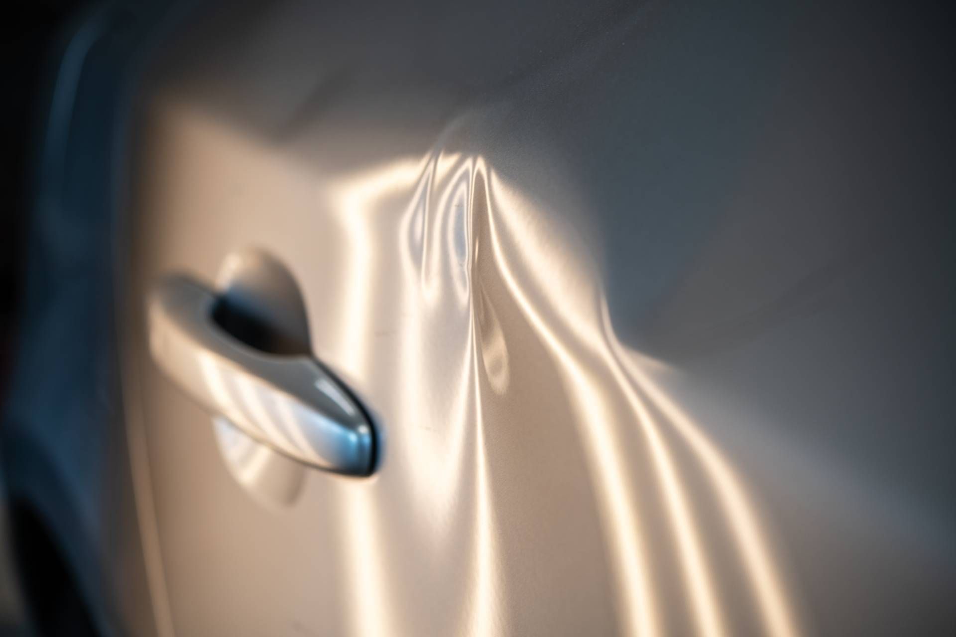 Close-up of a car door featuring multiple dents illuminated by soft lighting