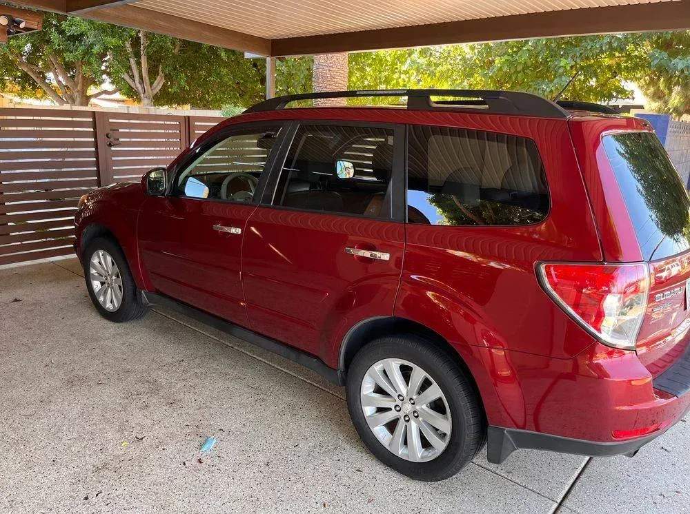 A red suv is parked under a canopy in a driveway.