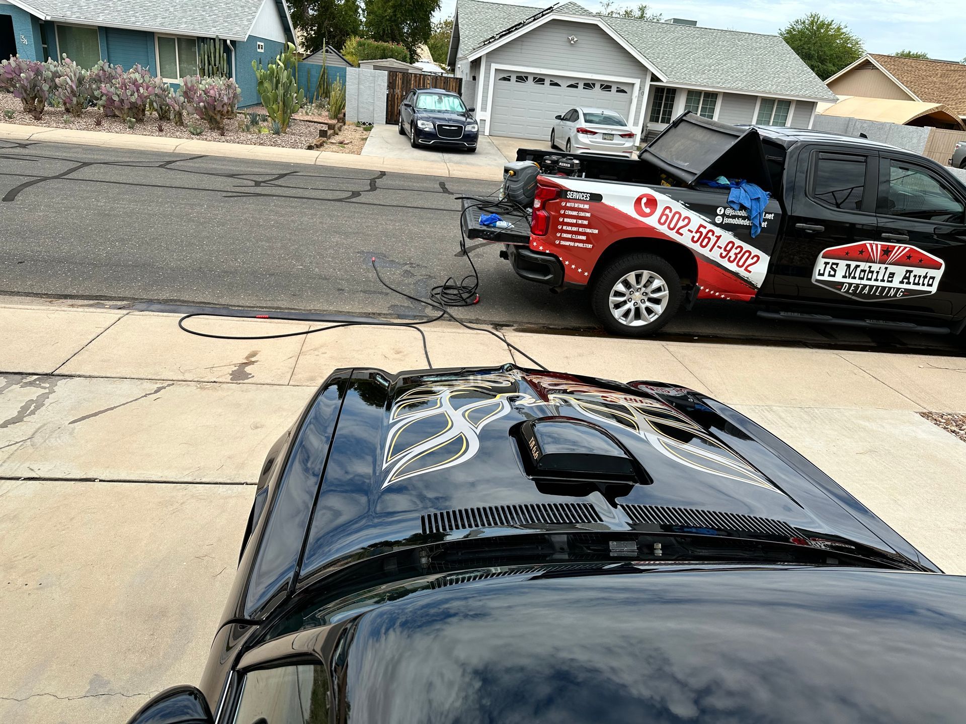 A black car is parked next to a red and white truck with a phone number on the back.
