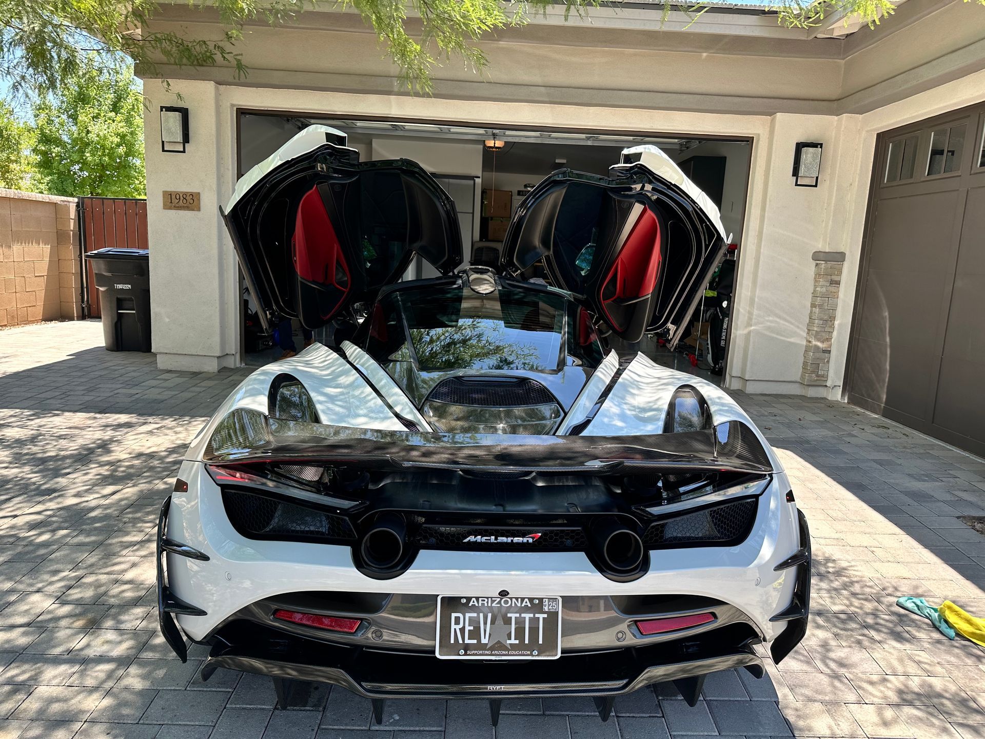 A white sports car is parked in a garage with its trunk open.