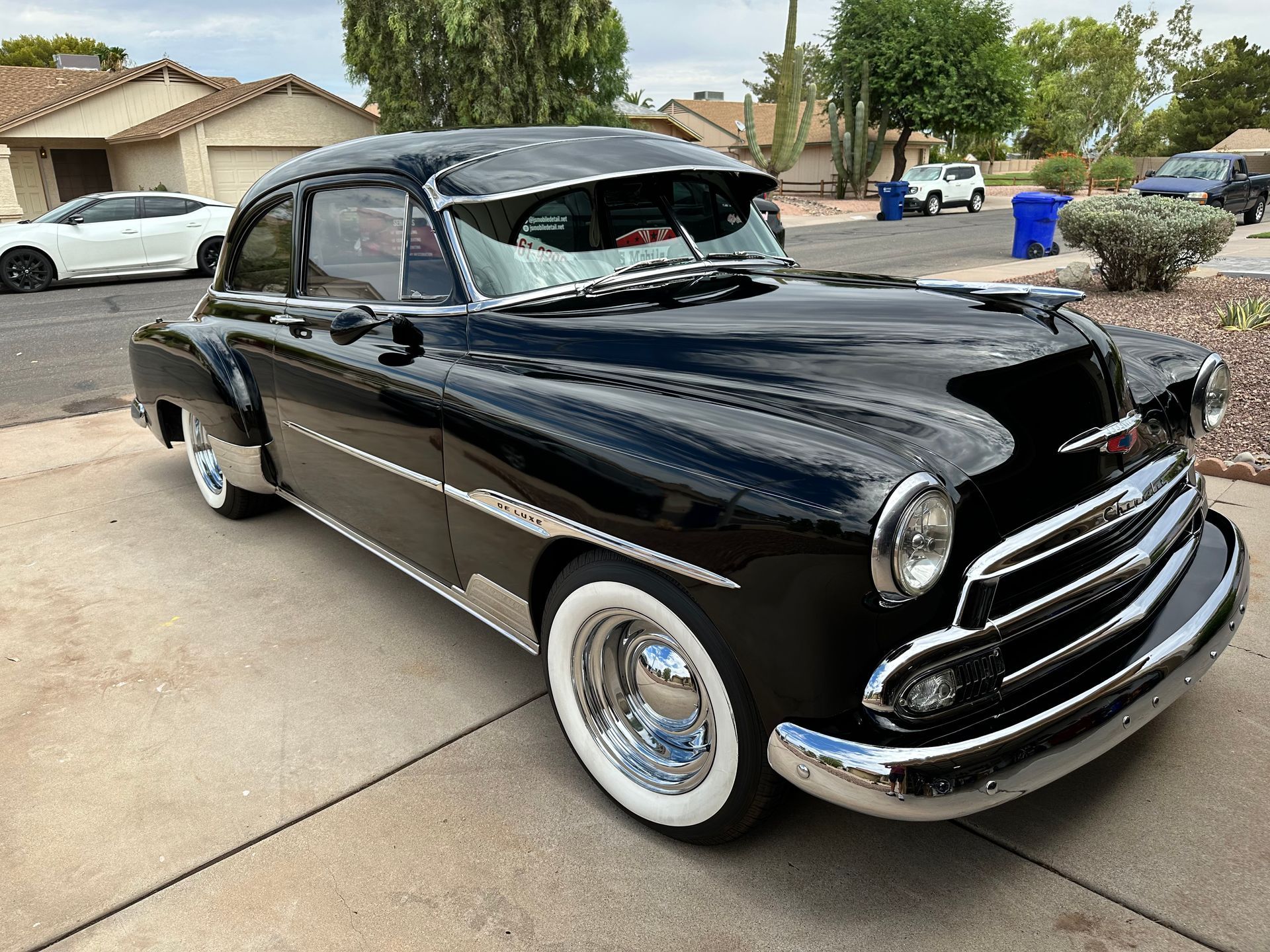 A black car with white tires is parked in a driveway.