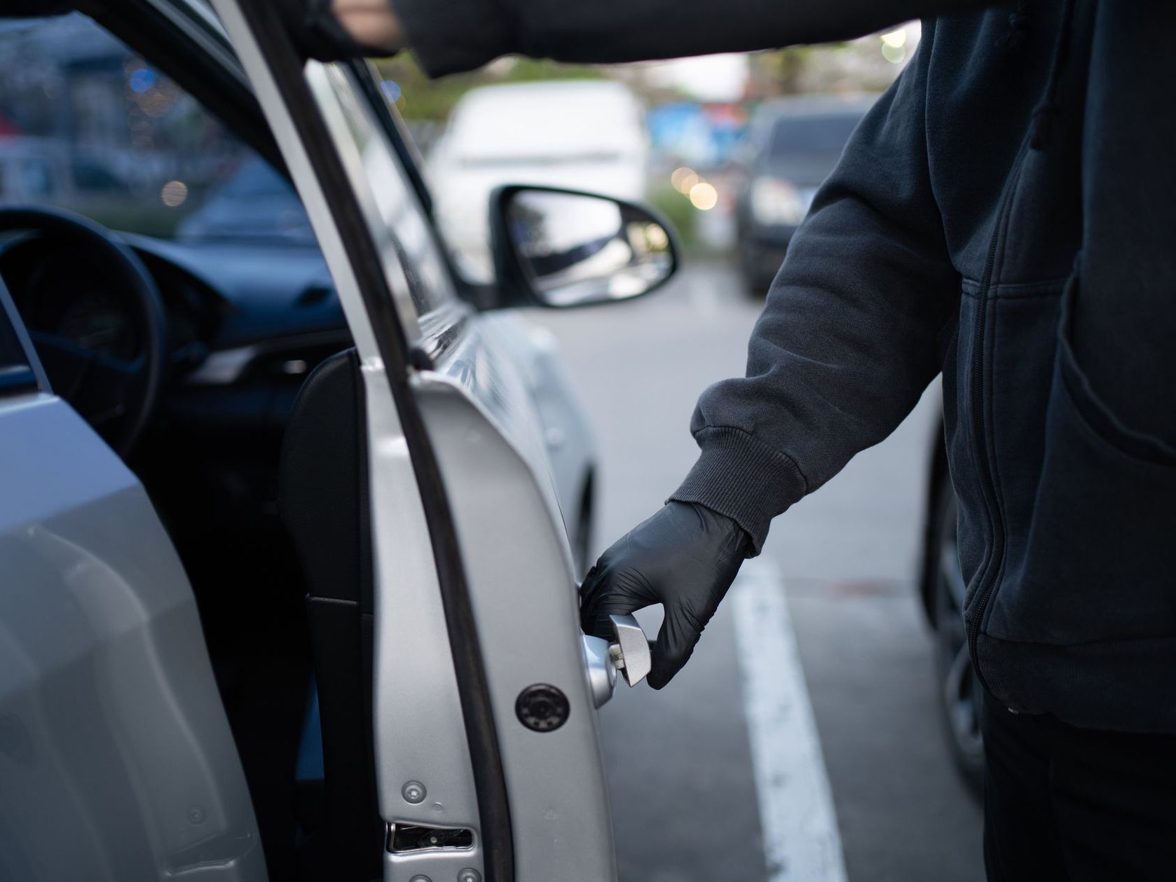 A man wearing black gloves is opening the door of a car.