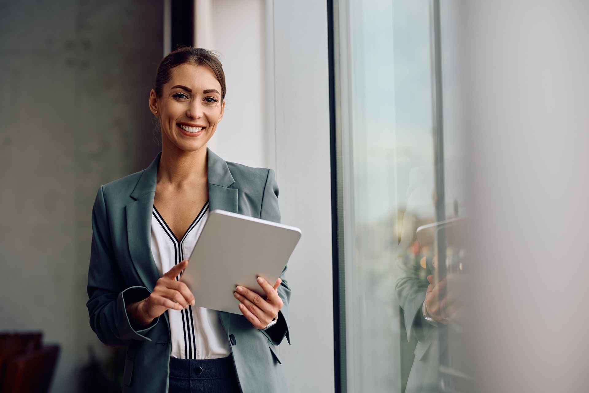 A woman is standing in front of a window holding a tablet computer.