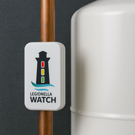 Legionella Watch device on copper pipe, showing a lighthouse traffic light graphic; white tank in background.
