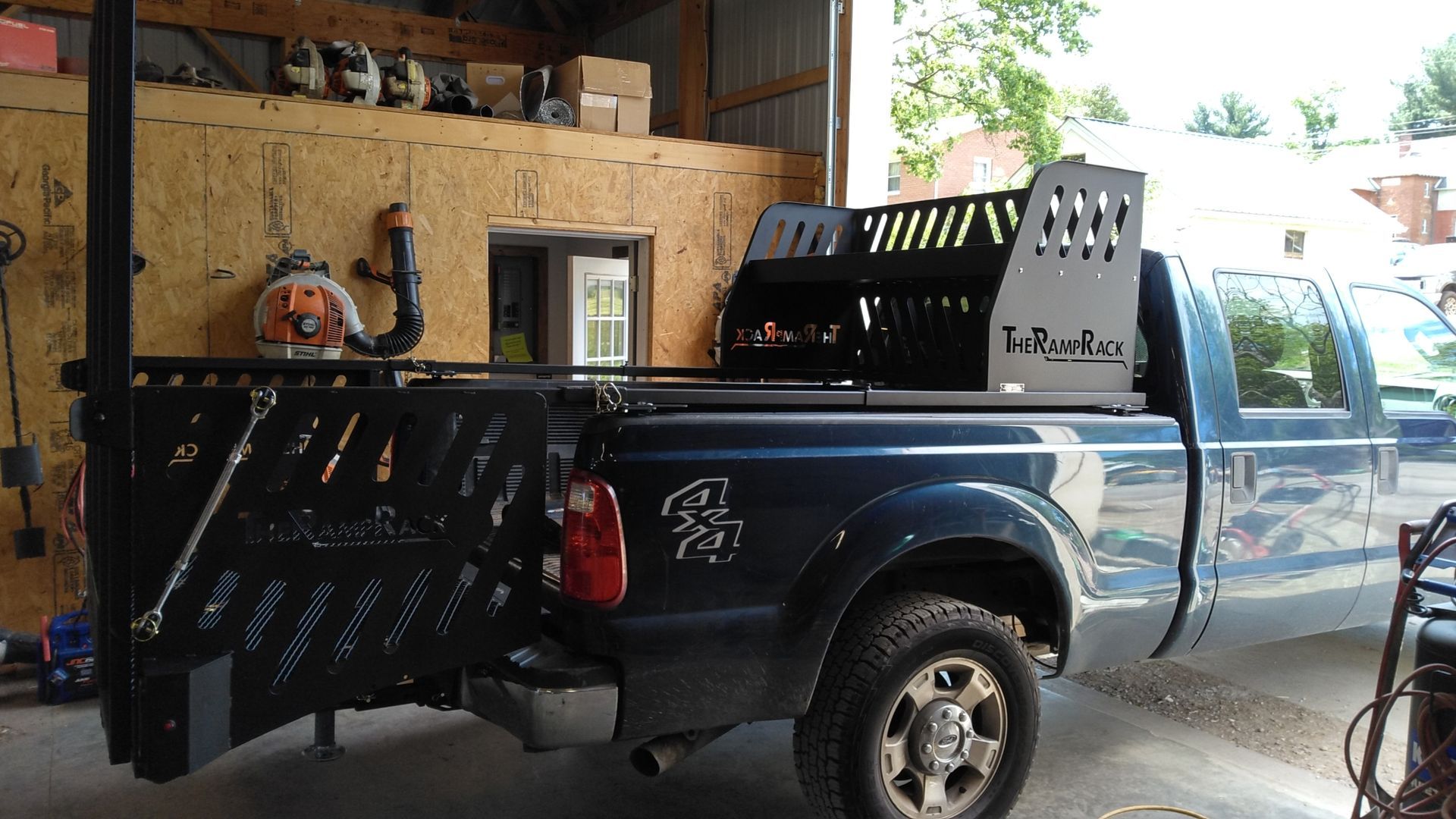 Blue pickup truck in a garage with a mounted black utility rack and open tailgate.