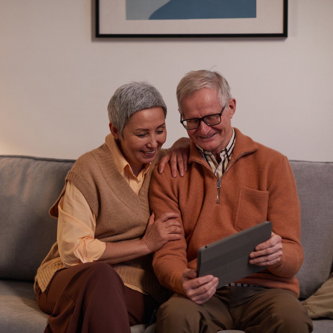 A man and woman are sitting on a couch looking at a tablet