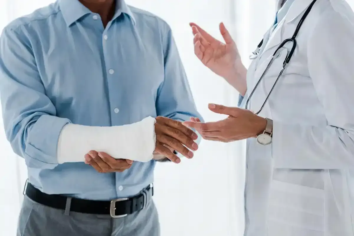 Uomo con un braccio ingessato che consulta un medico in un ambiente medico.