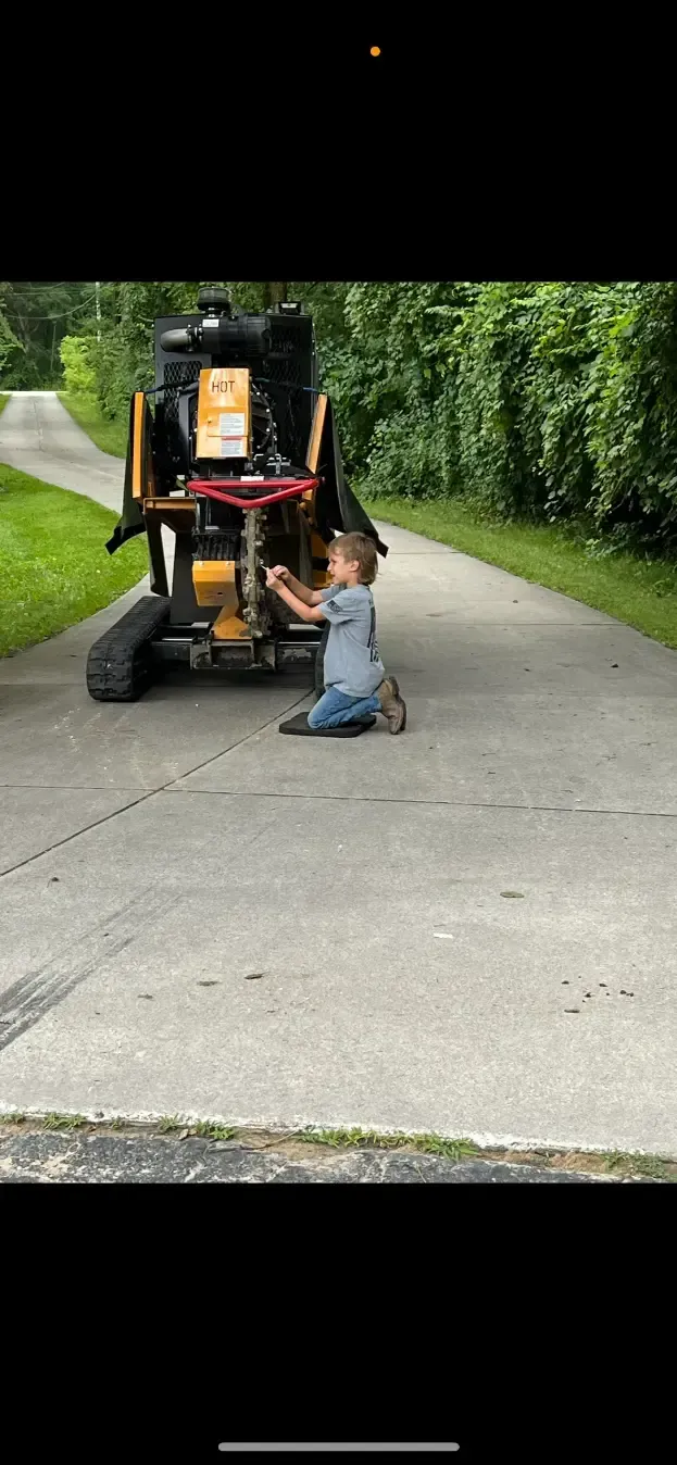 A little boy is kneeling down in front of a forklift.