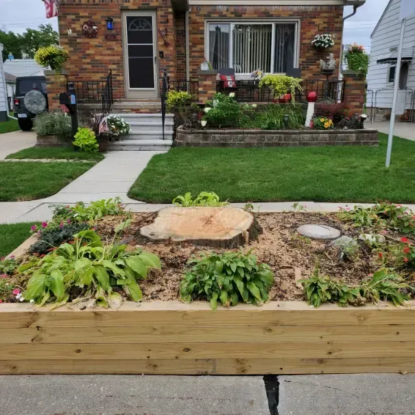A wooden planter with a tree stump in it is in front of a brick house.