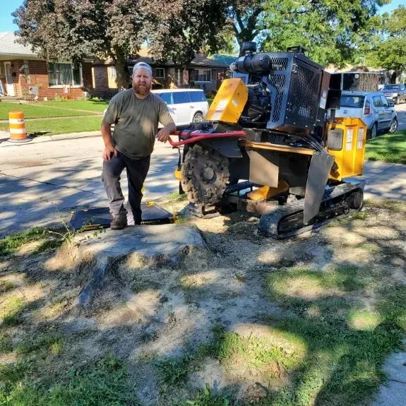 A man is standing next to a stump grinder on the side of the road.
