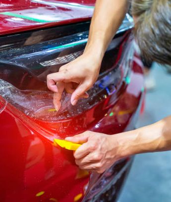 A person is applying protective film to a red car.