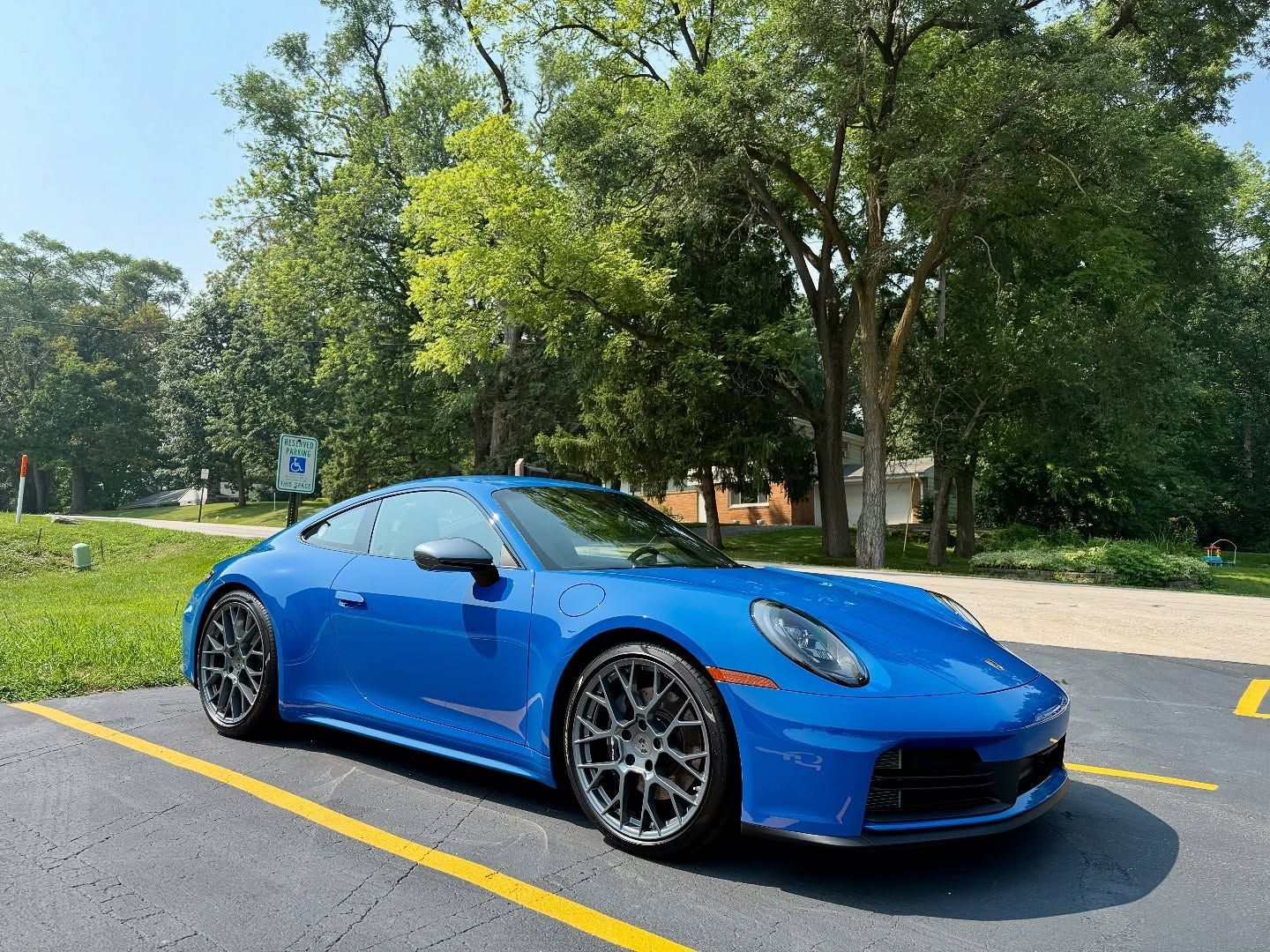 Blue sports car parked on a road beside a grassy park under sunny trees