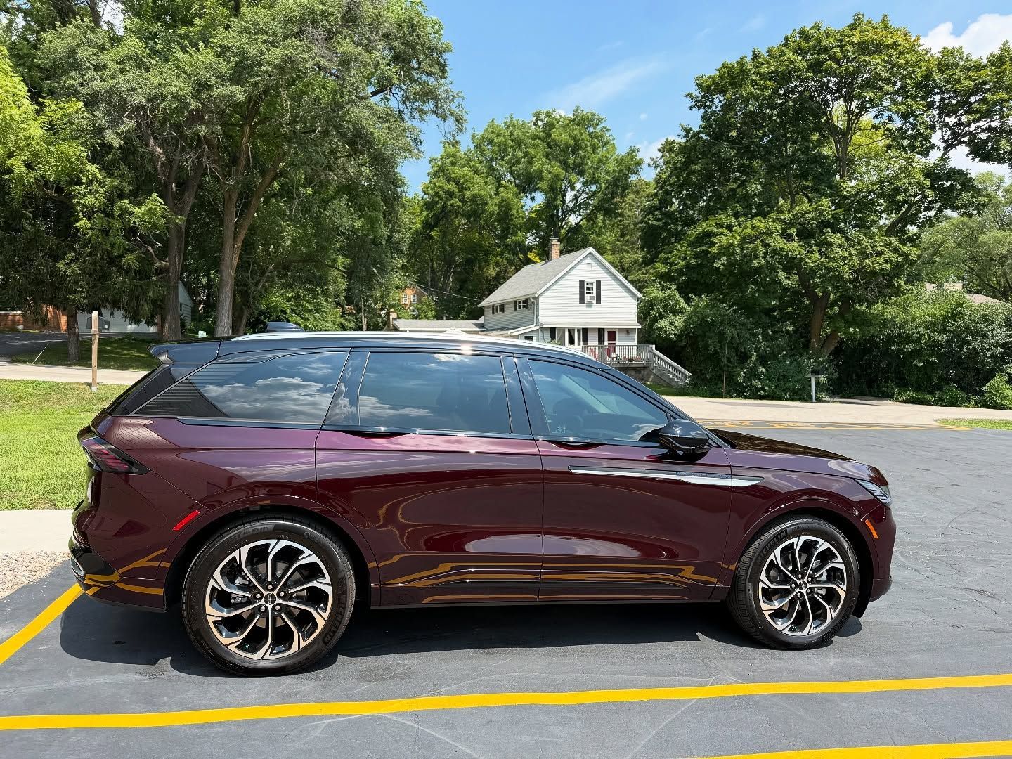 Maroon SUV parked in a lot near trees and a small white house on a sunny day