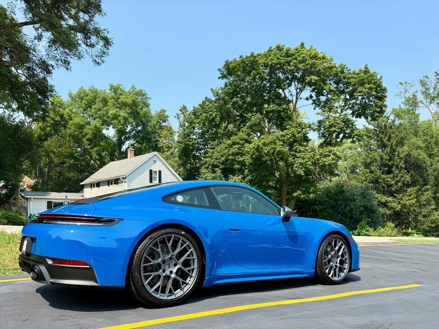 Bright blue sports car parked on a road with trees and a house in the background