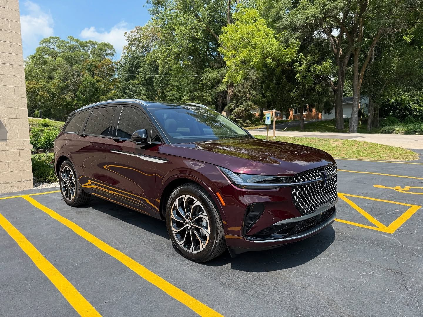 Maroon SUV parked in a lot near a building, with yellow no-parking lines and trees nearby