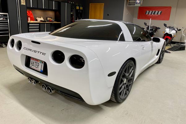 White Corvette coupe with custom wheels and license plate in a garage.