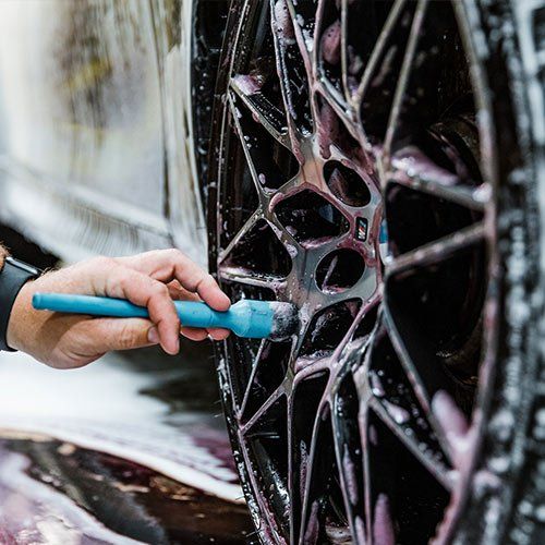 A person is cleaning a car wheel with a brush.
