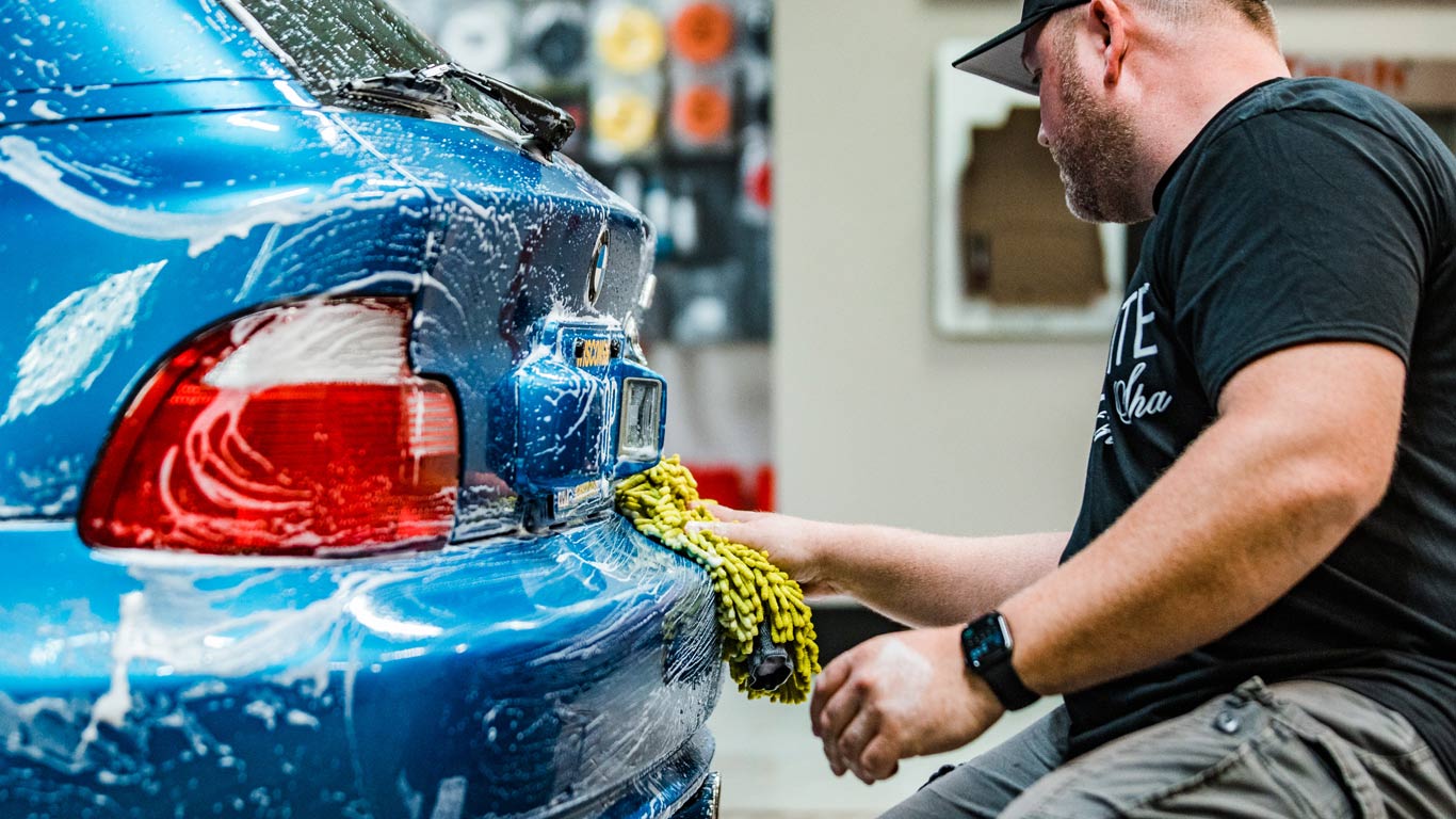 A man is washing a blue car in a garage.