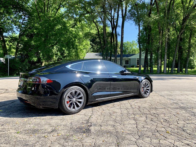 A black tesla model s is parked on the side of the road.