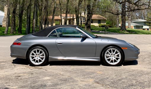 A silver porsche 911 convertible is parked in a parking lot.