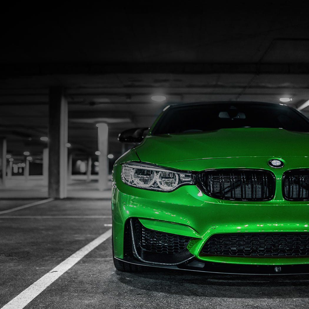A green bmw m4 is parked in a parking garage at night.
