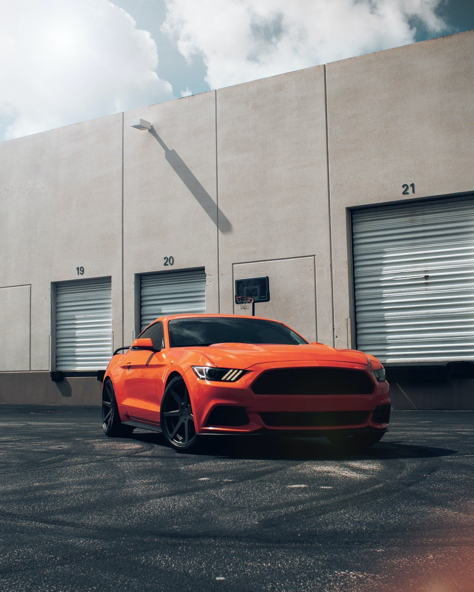 An orange mustang is parked in front of a building with garage doors.