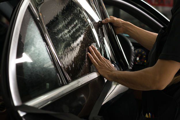 A person is applying tinted glass to a car window.