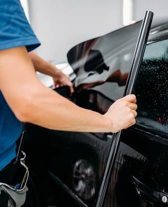 A man is applying window tinting to a black car.