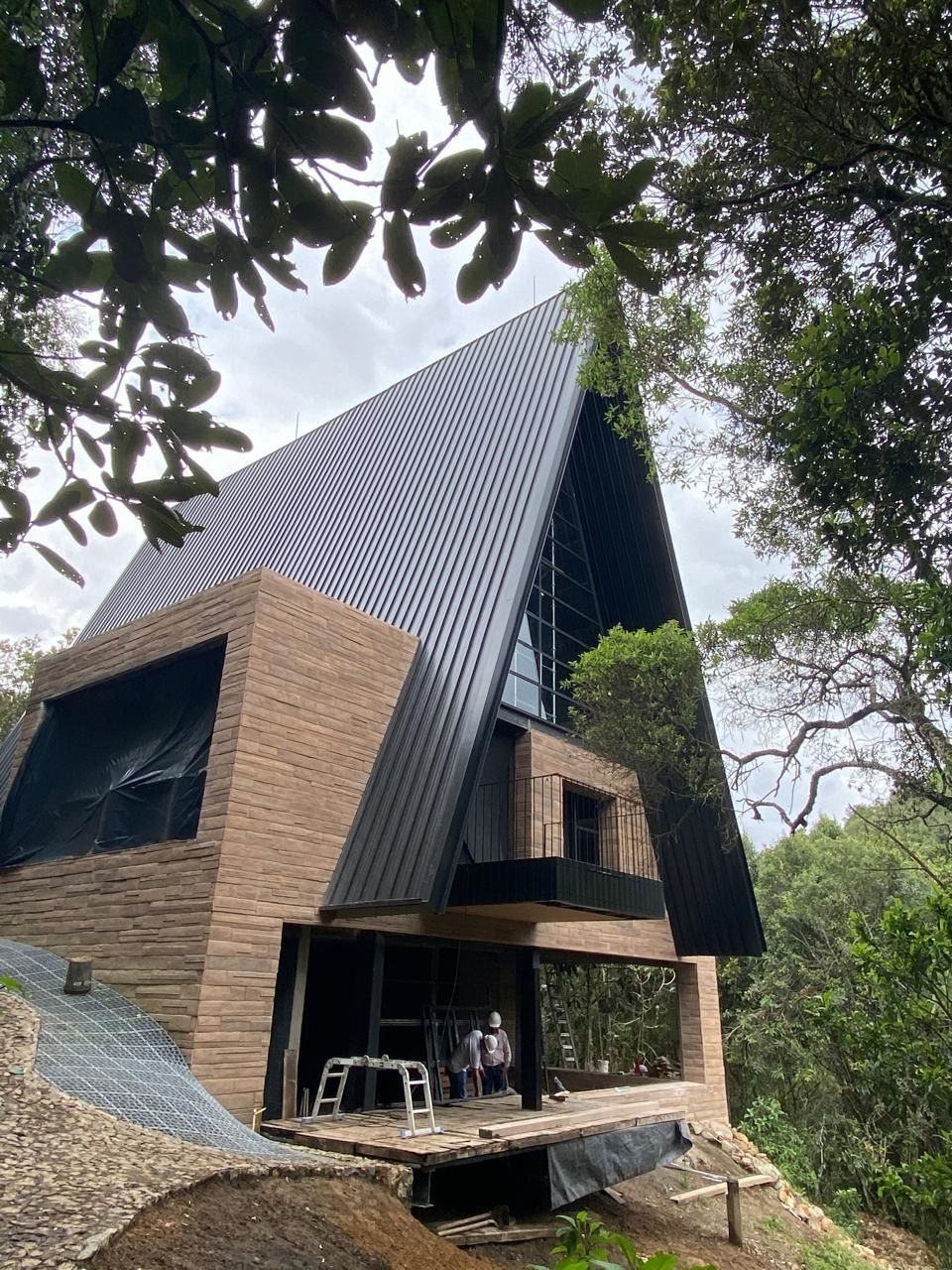 Se está construyendo una casa en una colina con árboles al fondo.