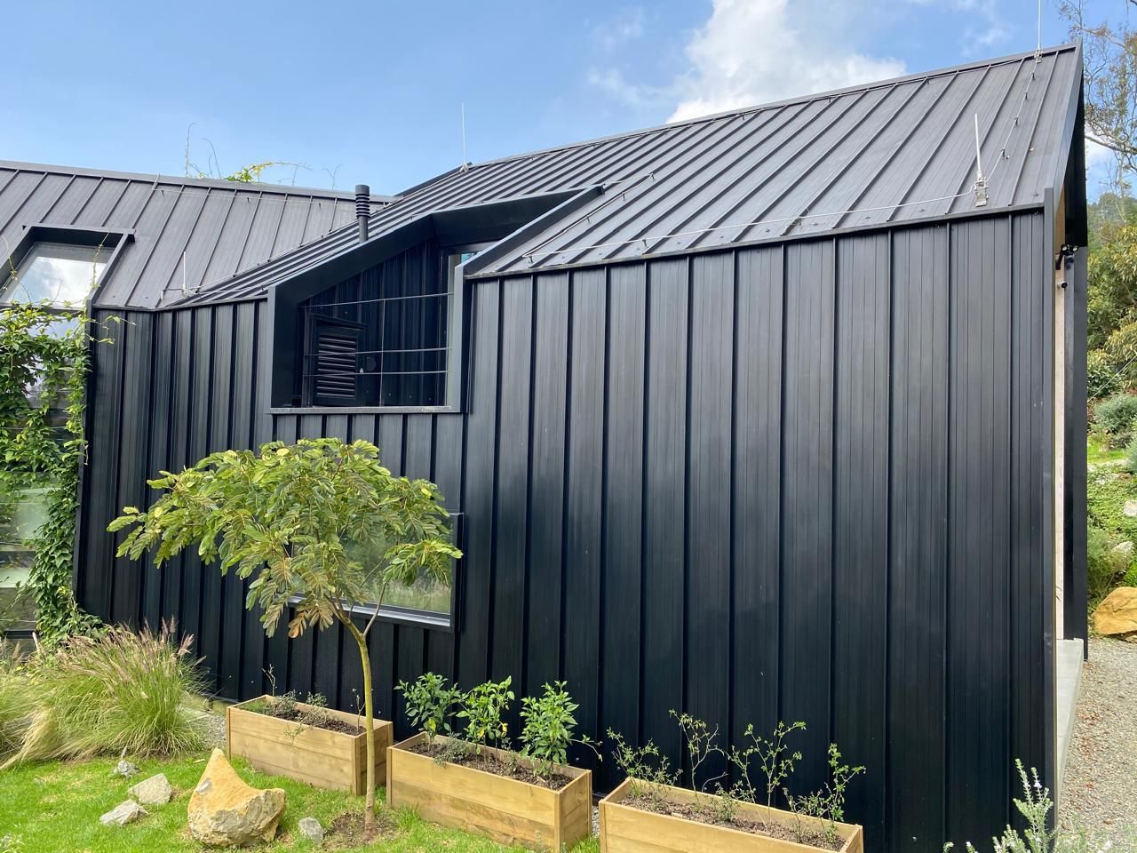 Una casa negra con techo negro se encuentra encima de un exuberante campo verde.
