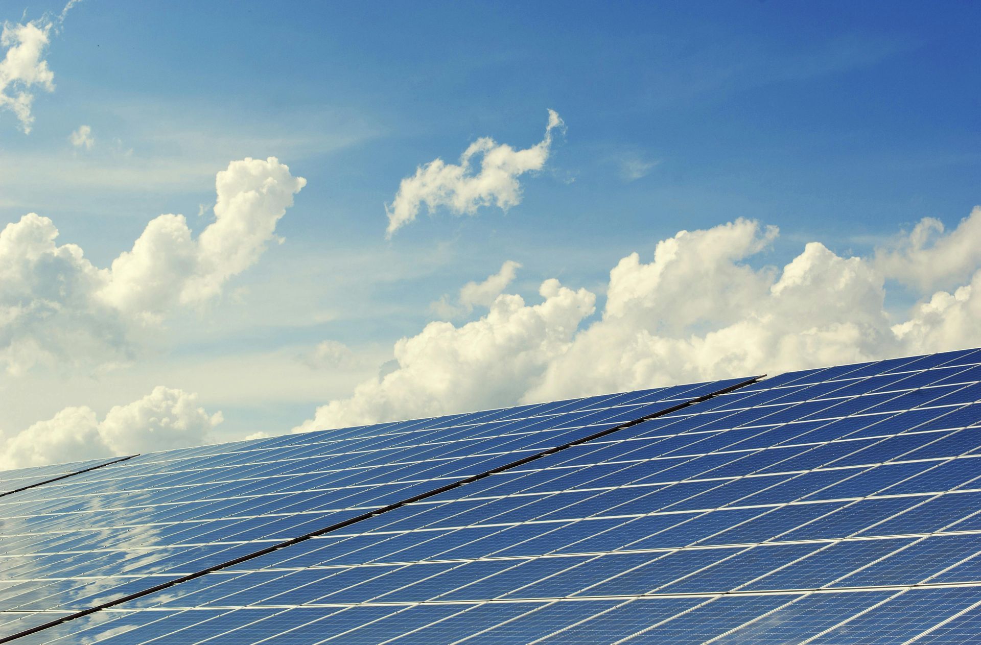 A row of solar panels against a blue sky with clouds.