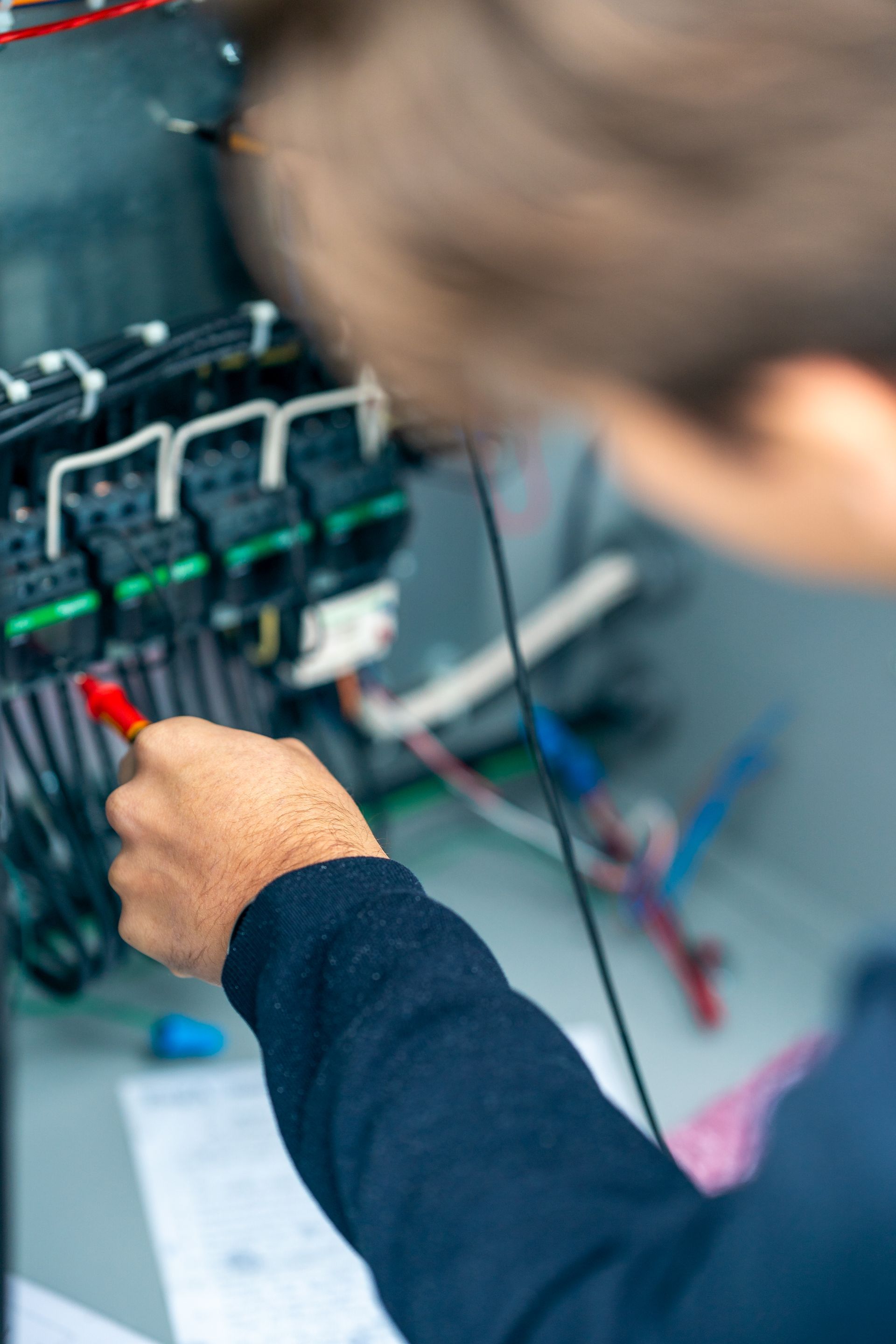 Person using a screwdriver to work on electrical wiring in a gray cabinet.