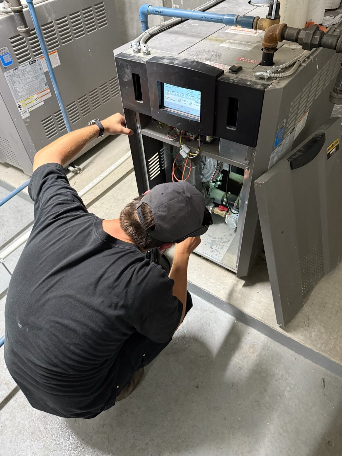 Person in a black shirt works on a machine in an industrial setting, with a screen and exposed wiring.