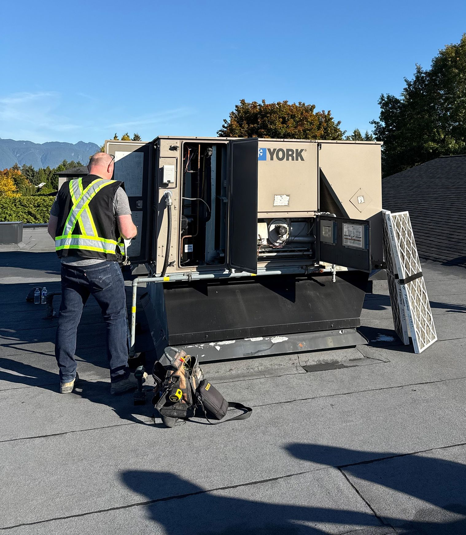 Two workers on a rooftop, one near a York HVAC unit, another working on the roof. Bright sunlight.