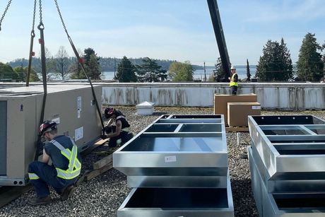Workers installing HVAC unit on a rooftop with crane.  Blue sky, lake in background.