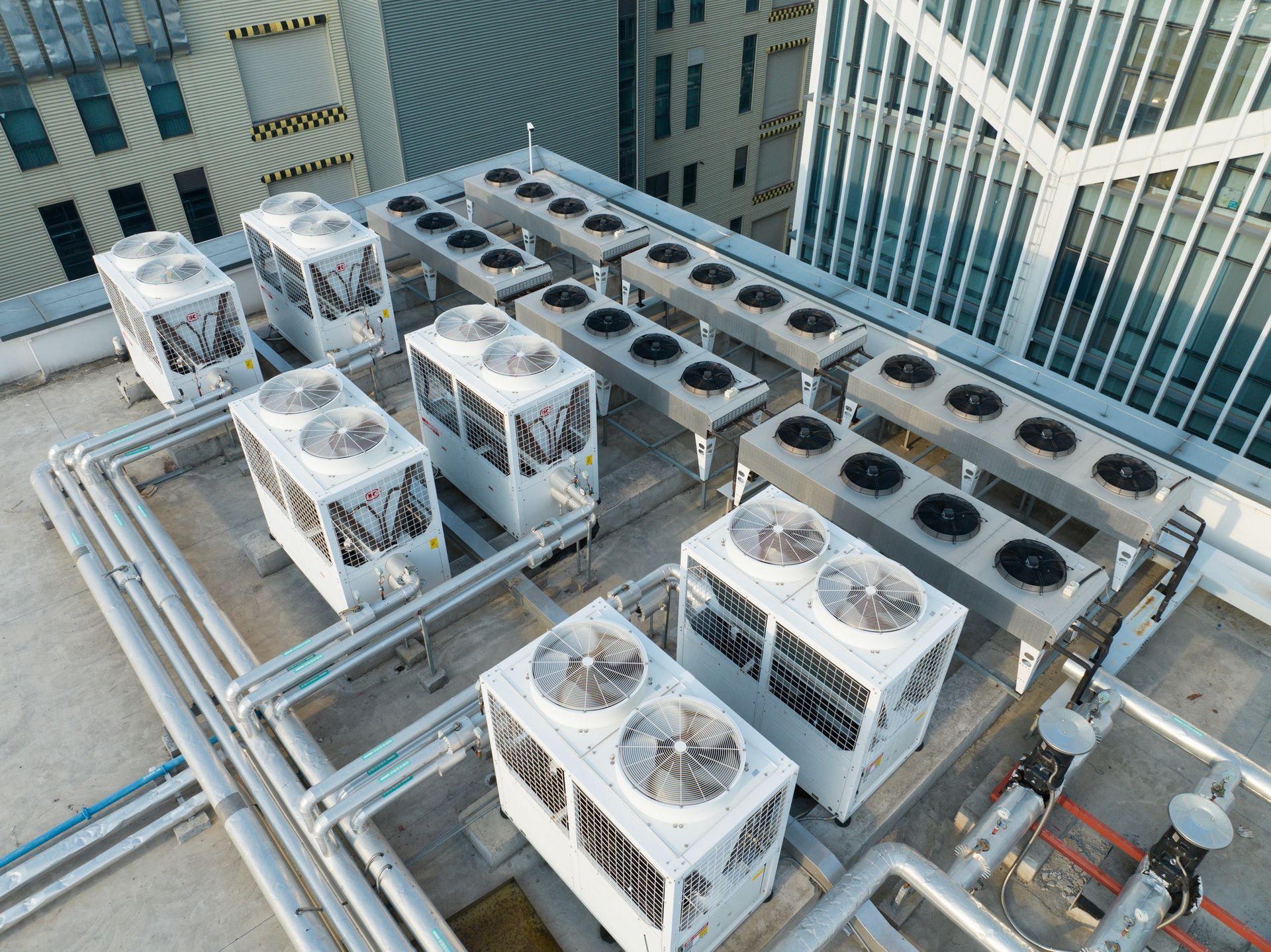 Rooftop with multiple air conditioning units and associated piping. The units are white with grey fans.