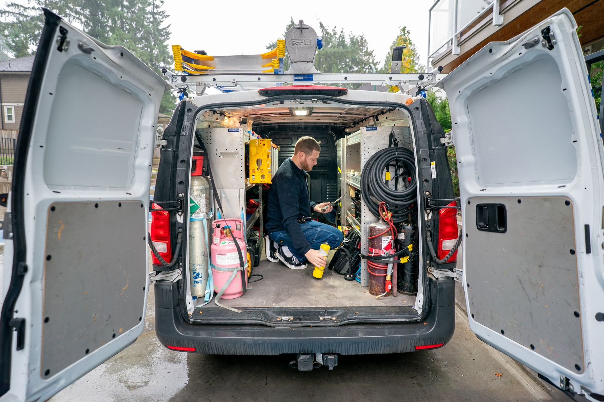 Plumber inspecting pipes inside a wall, kneeling with tools.
