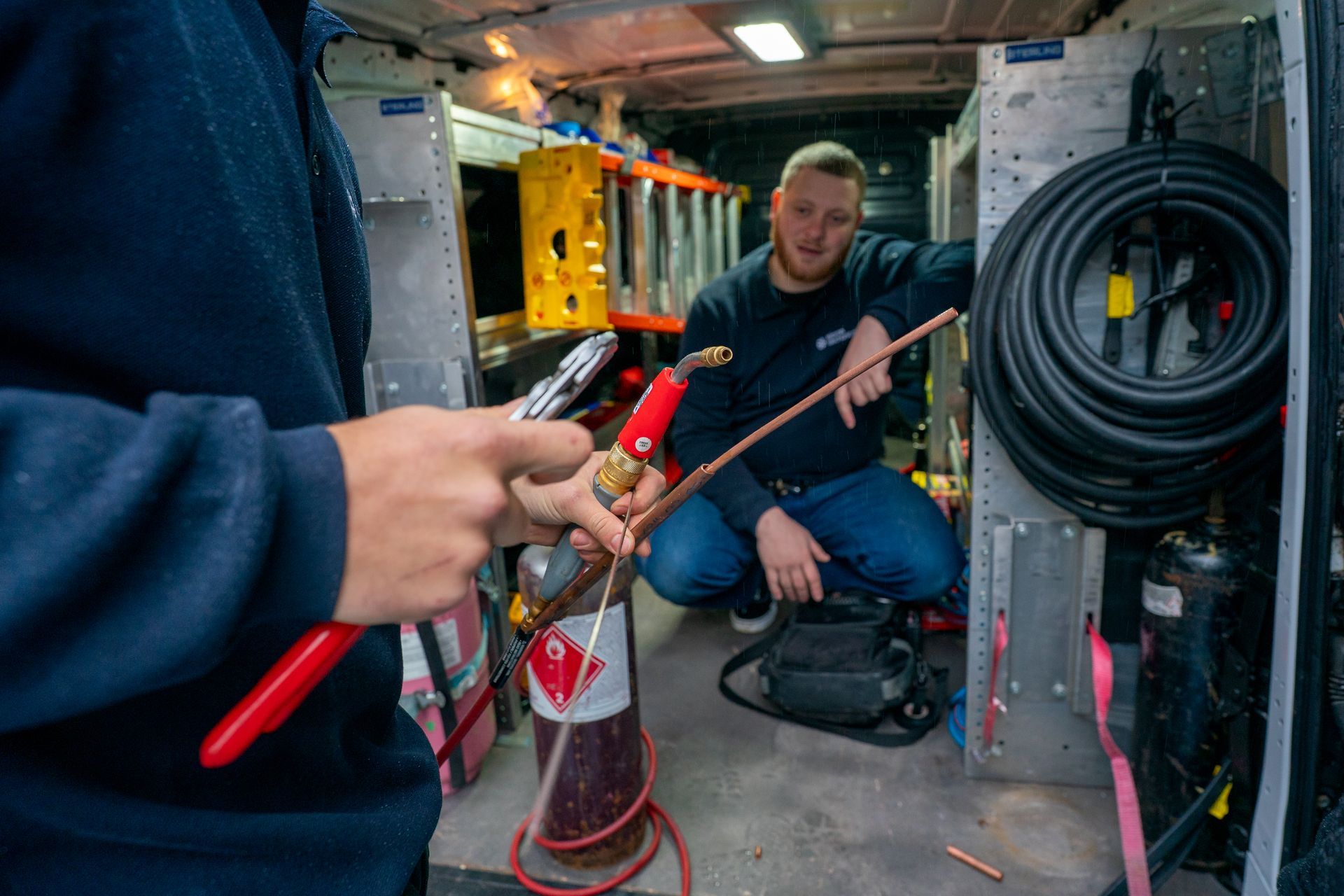 Air conditioning unit next to a house with a wooden deck and stairs, surrounded by greenery.