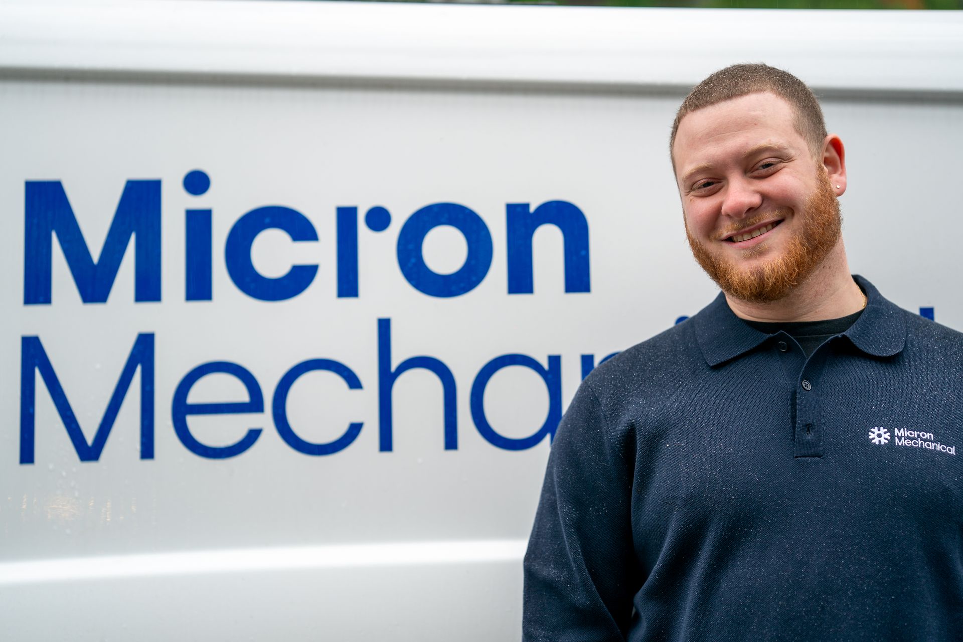Air conditioner unit outside a brown house near a wooden deck and foliage.