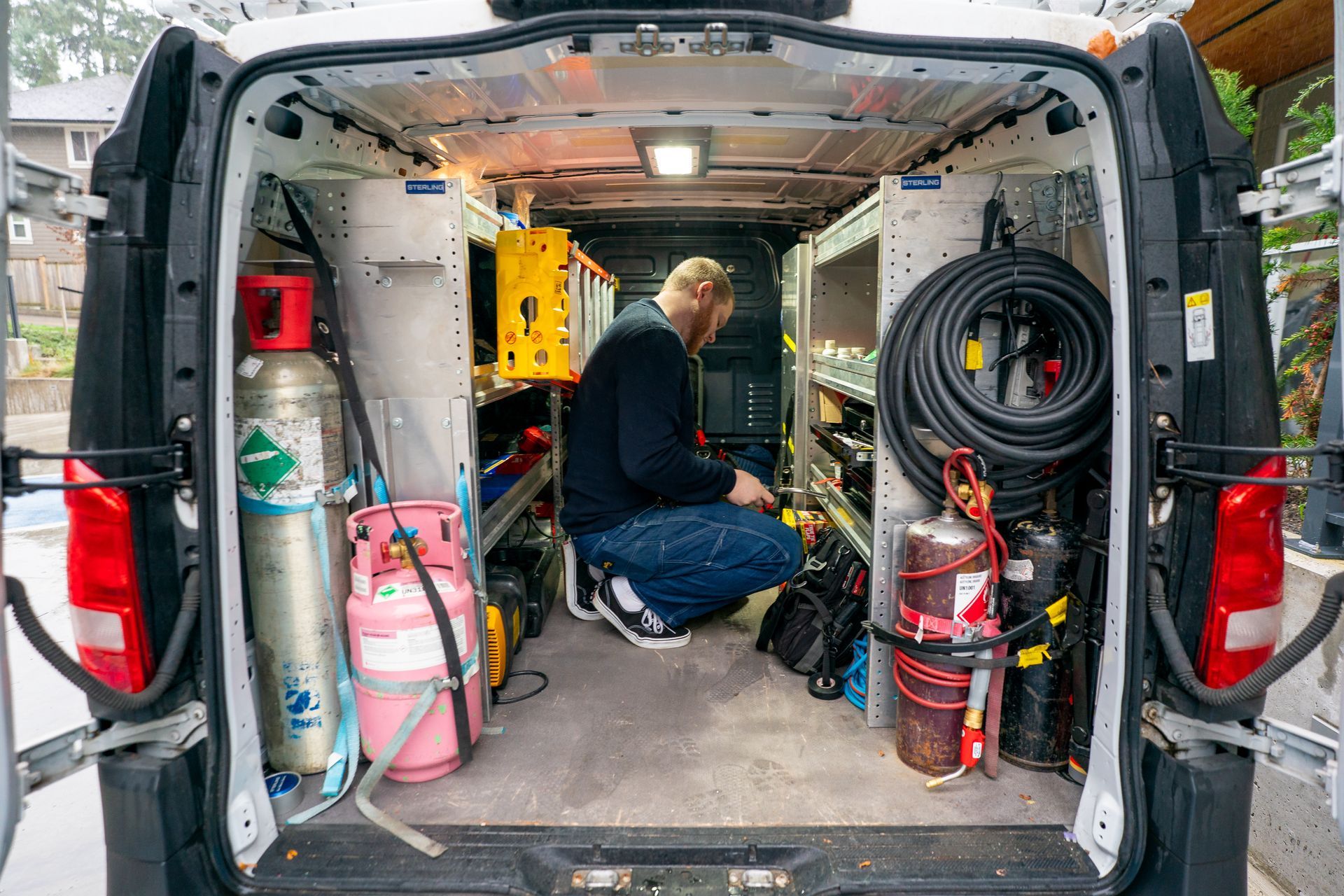 Air conditioning unit next to a house with a wooden deck and stairs, surrounded by greenery.