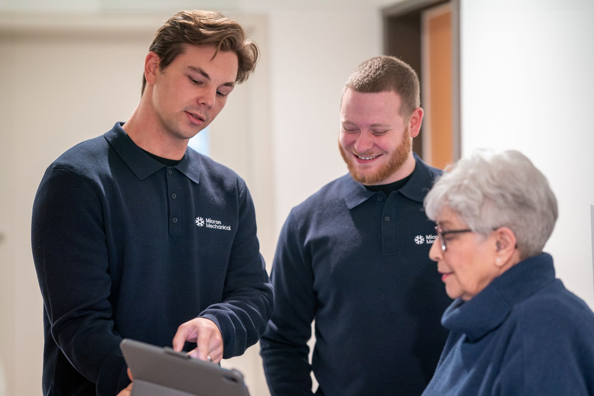 Air conditioning unit next to a house with a wooden deck and stairs, surrounded by greenery.