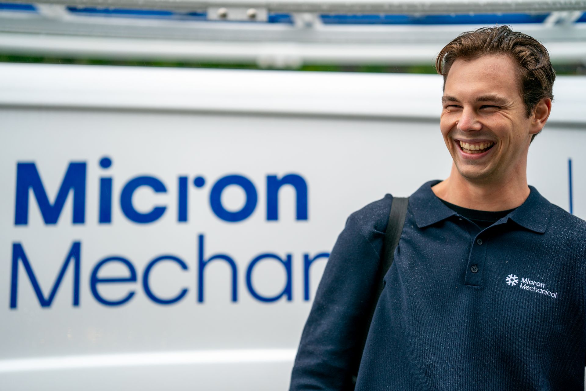 Air conditioning unit next to a house with a wooden deck and stairs, surrounded by greenery.