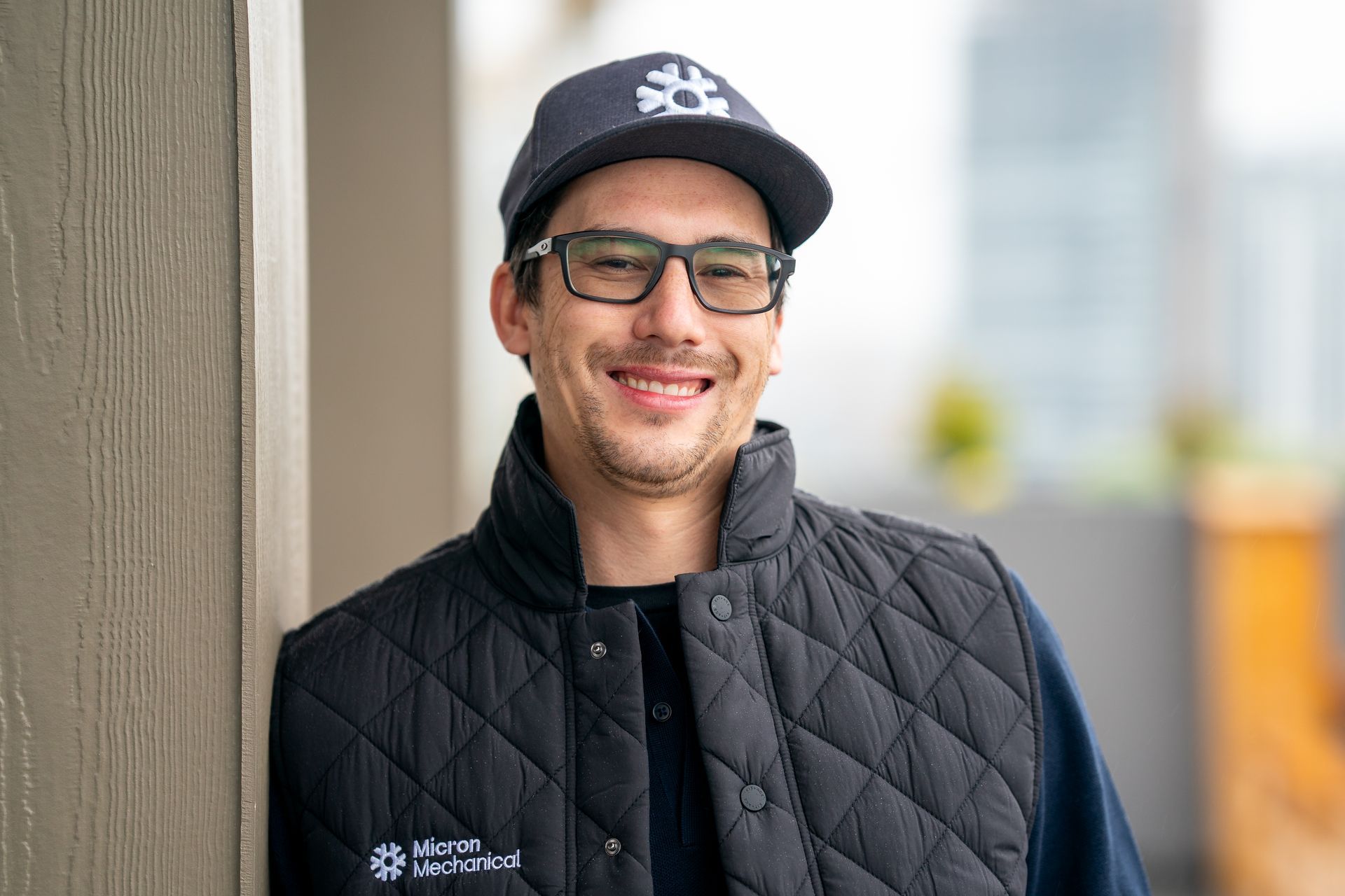 Air conditioning unit next to a house with a wooden deck and stairs, surrounded by greenery.