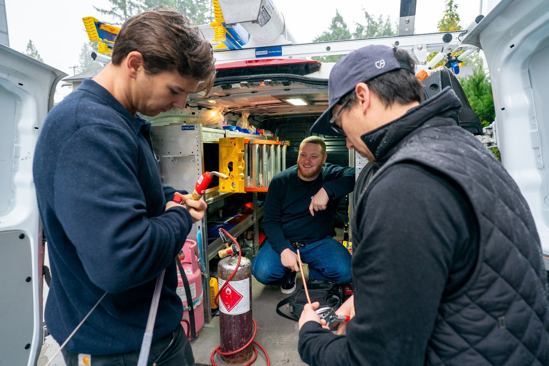 Air conditioning unit next to a house with a wooden deck and stairs, surrounded by greenery.