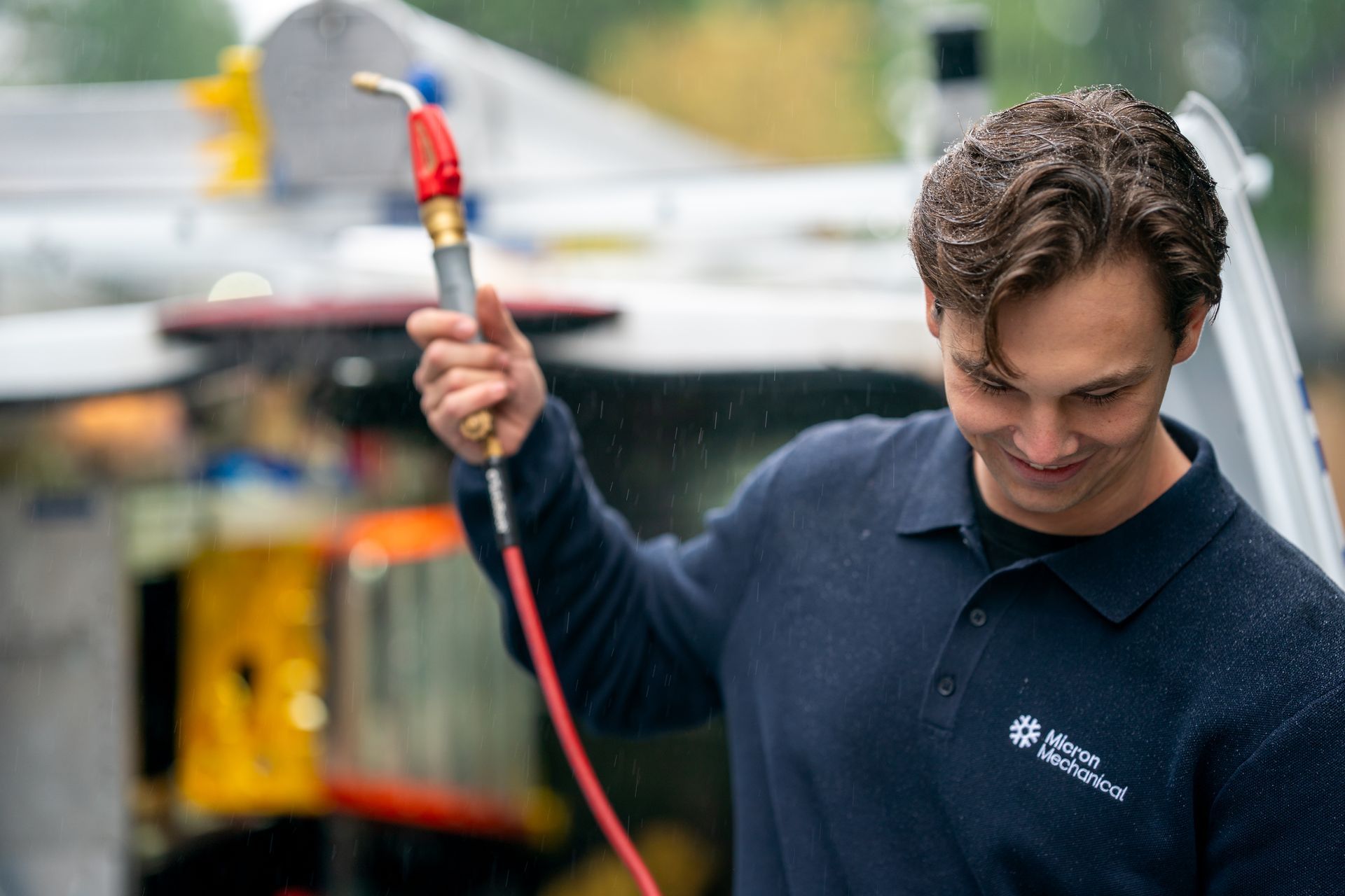 Air conditioner unit outside a brown house near a wooden deck and foliage.